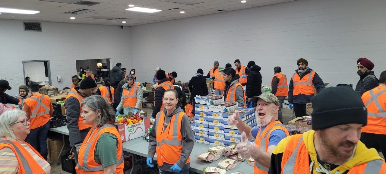 Volunteers in orange vests packing food at tables in the hall